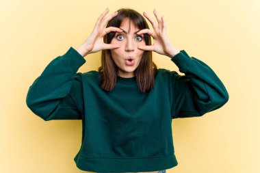 Sarı arka planda izole edilmiş genç beyaz kadın bir başarı fırsatı bulmak için gözlerini açık tutuyor..