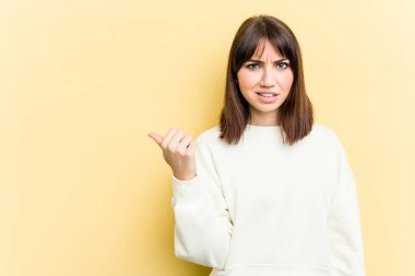 Sarı arka planda izole edilmiş genç beyaz kadın işaret parmağıyla fotokopi alanını işaret ederek şok oldu..