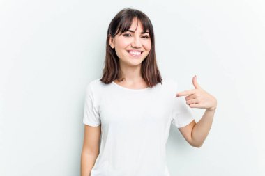 Beyaz arka planda yaşayan beyaz tenli genç bir kadın gömlek fotokopi alanını elle işaret ediyor, gururlu ve kendinden emin