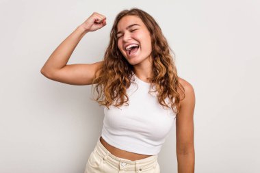 Mavi arka planda izole edilmiş genç beyaz kadın zaferi, tutkuyu ve coşkuyu kutluyor, mutlu bir ifade..