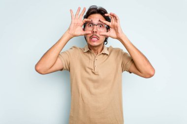 Genç İspanyol bir adam mavi arka planda izole edilmiş. Başarı fırsatı bulmak için gözlerini açık tutuyor..