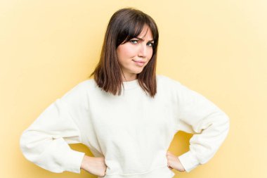 Sarı arka planda izole edilmiş, hoşnutsuzca kaşlarını çatmış, kollarını kavuşturmuş genç beyaz bir kadın..