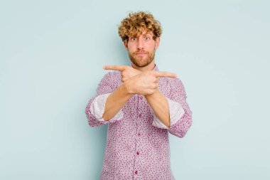 Mavi arka plan noktalarında izole genç beyaz adam, iki seçenek arasında seçim yapmaya çalışıyor.