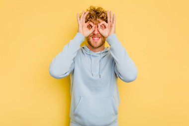 Sarı arka planda izole edilmiş genç beyaz adam gözlerinde sorun olmadığını gösteriyor.