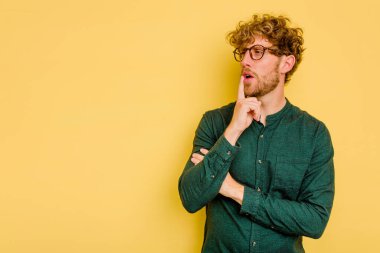 Sarı arka planda izole edilmiş genç beyaz adam şüpheli ve şüpheci bir ifadeyle yana bakıyor..