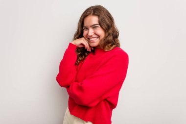 Mavi arka planda izole edilmiş genç beyaz kadın mutlu ve kendinden emin gülümsüyor, elleriyle çenesine dokunuyor..