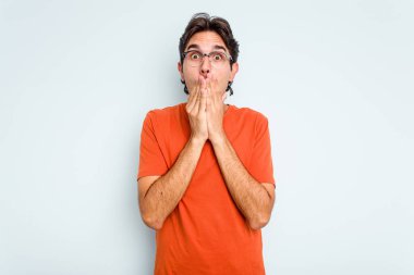 Mavi arka planda izole edilmiş genç İspanyol adam elleriyle ağzını kapatırken şok oldu..