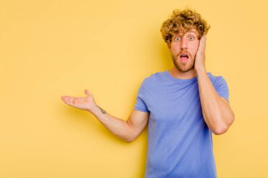 Sarı arka planda izole edilmiş genç beyaz adam, avuç içi fotokopi alanını elinde tutmaktan etkilendi..