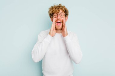 Kafkasyalı genç adam mavi arka planda izole edilmiş. Dedikodu yapıyor, bir şeyleri bildiriyor..