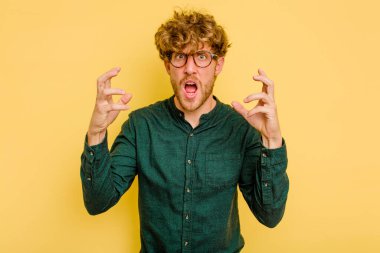 Sarı arka planda izole edilmiş genç beyaz adam öfkeyle bağırıyor..