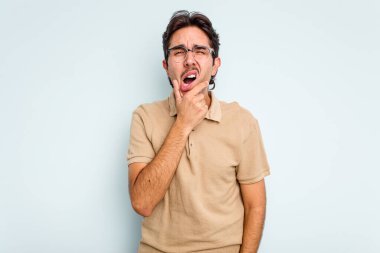 Genç İspanyol bir adam mavi arka planda izole edilmiş güçlü bir diş ağrısı, azıdişi ağrısı var..