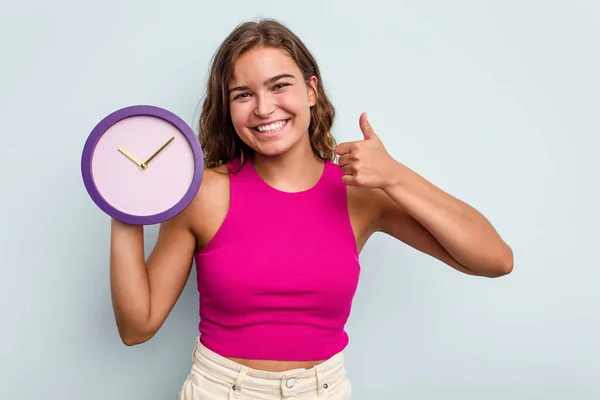Joven Mujer Caucásica Sosteniendo Reloj Aislado Sobre Fondo Azul Sonriendo —  Fotos de Stock
