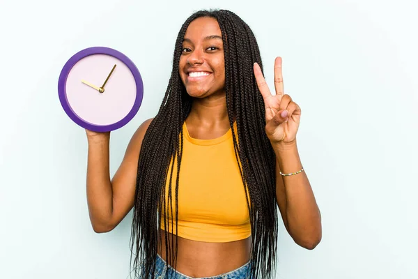 Молодая Афроамериканка Держит Часы Синем Фоне Показывая Номер Два Пальцами — стоковое фото