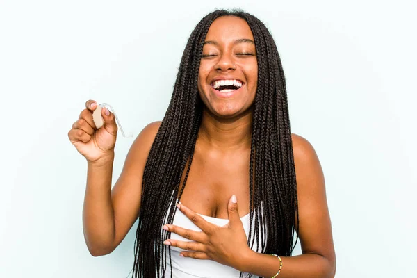 若いアフリカ系アメリカ人女性は青い背景で隔離された補聴器を持っています笑大声で胸に手を保つ — ストック写真