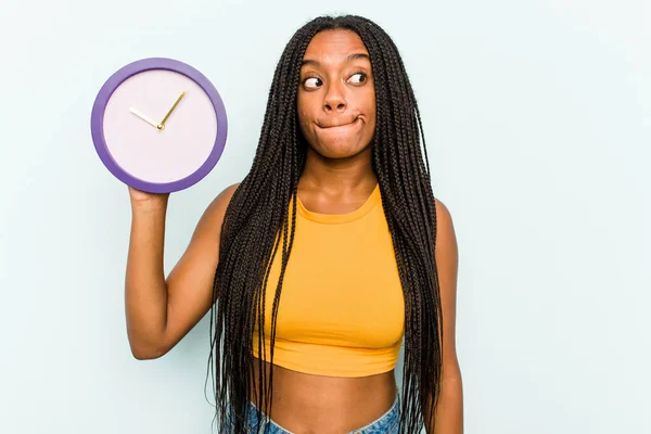 Ung Afroamerikansk Kvinna Som Håller Klocka Isolerad Blå Bakgrund Förvirrad — Stockfoto