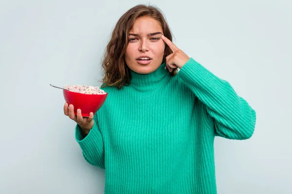 年轻的高加索女人拿着一碗谷物 蓝色背景隔离 用食指表示失望的姿态 — 图库照片