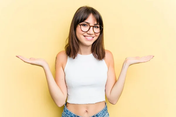 Young Caucasian Woman Isolated Yellow Background Makes Scale Arms Feels — Stock Photo, Image