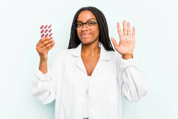 年轻的非洲裔美国女药剂师 身披蓝色背景 开开朗地微笑着 用手指展示第五位 — 图库照片