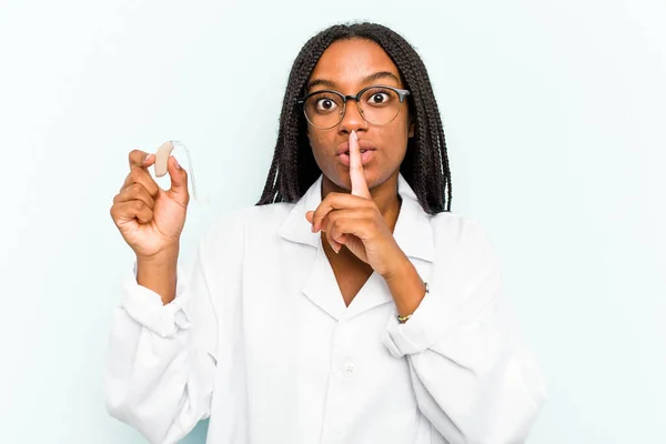 Young African American Otorhinolaryngologist Woman Holding Hearing Aid Isolated Blue — Stock Photo, Image