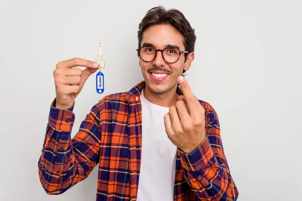 年轻的惊慌失措的男人拿着家里的钥匙 被白色的背景隔开 用手指指著你 好像在邀请你走近 — 图库照片