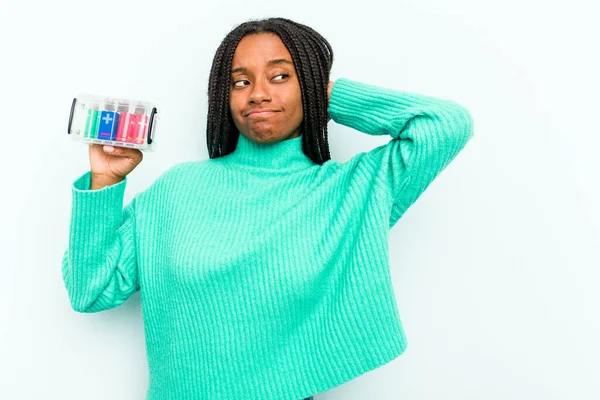 若いアフリカ系アメリカ人の女性は 頭の後ろに触れる青い背景に隔離されたバッテリーボックスを保持し 選択をする — ストック写真