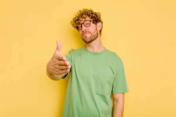 Jovem Caucasiano Isolado Fundo Amarelo Esticando Mão Câmera Gesto Saudação — Fotografia de Stock