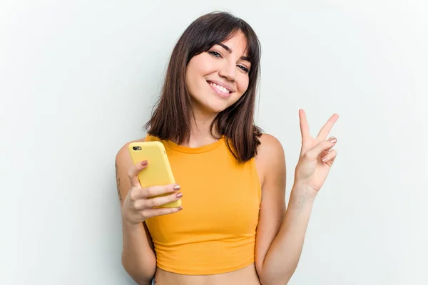 年轻的高加索女人用白色背景隔离的手机快乐而无忧无虑地用手指展示和平的象征 — 图库照片