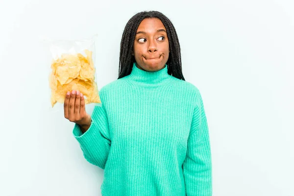 Jonge Afro Amerikaanse Vrouw Houdt Chips Geïsoleerd Blauwe Achtergrond Verward — Stockfoto