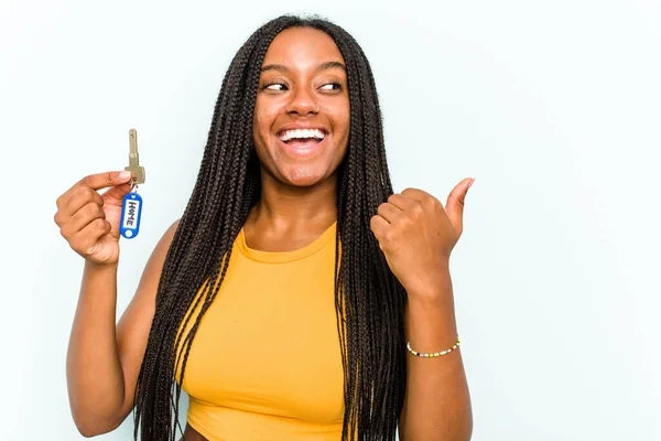 年轻的非洲裔美国女人拿着一把家庭钥匙 被蓝色的背景点隔开 无忧无虑地拿开大拇指 笑逐颜开 — 图库照片