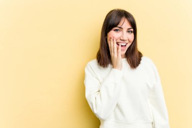Sarı arka planda izole edilmiş genç beyaz kadın yüksek sesle bağırıyor, gözleri açık ve elleri gergin tutuyor..