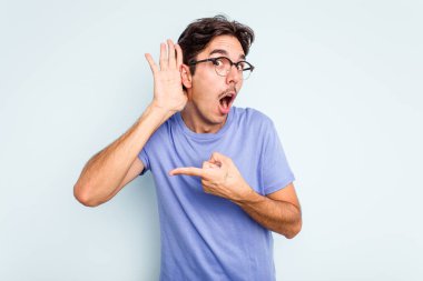 Genç İspanyol bir adam mavi arka planda izole edilmiş bir şekilde bir dedikoduyu dinlemeye çalışıyor..