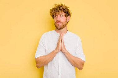 Kafkasyalı genç adam sarı arka planda izole edilmiş dua ediyor, bağlılık gösteriyor, dindar biri ilahi ilham arıyor..