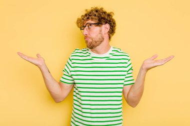 Kafkasyalı genç adam sarı arka planda izole edilmiş. Kafası karışmış ve omuz silkiyor. Kopya alanını tutmak için..