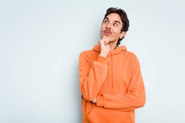 Genç İspanyol adam mavi arka planda izole edilmiş şüpheli ve şüpheci bir ifadeyle yana bakıyor..