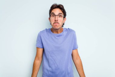 Mavi arka planda izole edilmiş genç bir İspanyol omuz silker ve gözleri açık kalır..