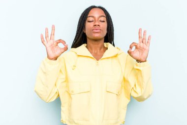 Mavi arka planda saç örgüsü olan genç Afrikalı Amerikalı kadın sıkı çalışma gününden sonra dinleniyor, yoga yapıyor..