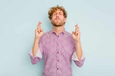 Kafkasyalı genç adam mavi arka planda izole edilmiş şans dilemek için şans diliyor.
