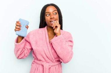 Mavi arka planda sünger tutan genç Afrikalı Amerikalı kadın rahatça fotokopi odasına bakan bir şey düşünüyor..