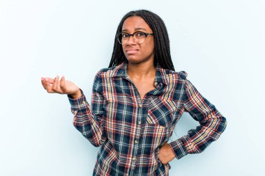 Saçları mavi arka planda izole edilmiş genç Afrikalı Amerikalı kadın sorgulama sırasında omuz silkiyor ve şüpheye düşüyor..