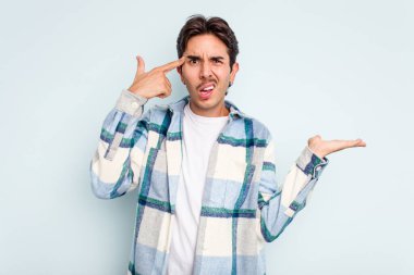 Genç İspanyol bir adam mavi arka planda izole edilmiş ve elinde bir ürün tutuyor..