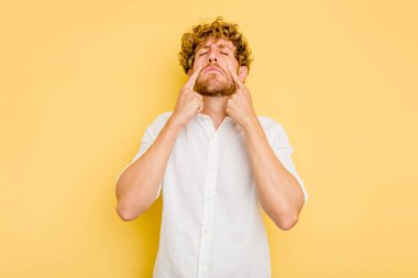 Kafkasyalı genç adam sarı arka planda izole edilmiş, ağlıyor, bir şeyden memnun değil, acı ve kafa karışıklığı kavramı..
