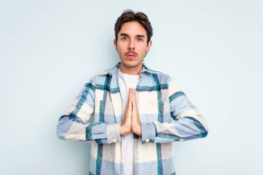 Genç İspanyol adam mavi arka planda izole edilmiş dua ediyor, bağlılık gösteriyor, dindar biri ilahi ilhamı arıyor..