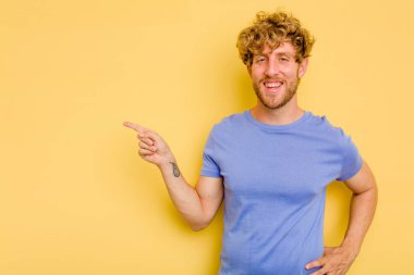 Sarı arka planda izole edilmiş genç beyaz adam işaret parmağıyla işaret ederek gülümsüyor..