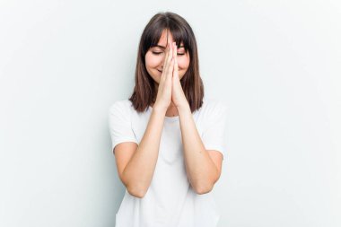Beyaz arka planda izole edilmiş genç beyaz bir kadın el ele dua ederken, kendine güveniyor..