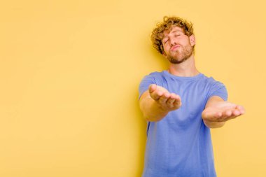 Sarı arka planda izole edilmiş genç, beyaz bir adam. Dudaklarını kıvırıyor, avuç içlerini tutuyor ve hava öpücüğü yolluyor..