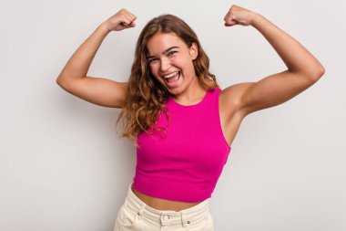 Mavi arka planda izole edilmiş genç beyaz kadın güçlü bir hareket sergiliyor kollarıyla, kadınsı gücün sembolü.