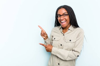 Mavi arka planda saçları olan genç Afrikalı Amerikalı kadın işaret parmaklarıyla işaret ederek heyecanlanıyor..