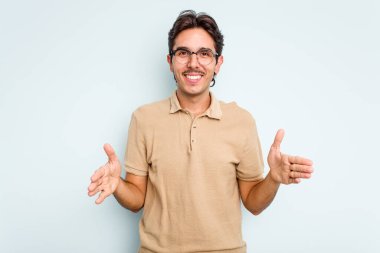 Mavi arka planda izole edilmiş genç İspanyol adam iki eliyle bir şey tutuyor, ürün sunumu..