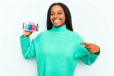 Genç Afrikalı Amerikalı bir kadın elinde batarya kutusuyla mavi arka planda yalnız başına gömlek fotokopi alanını işaret ediyor, gururlu ve kendinden emin.