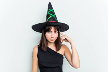 Beyaz arka planda izole edilmiş cadı gibi giyinmiş genç beyaz bir kadın. Parmağıyla tapınağı işaret ediyor, düşünüyor, bir göreve odaklanıyor..